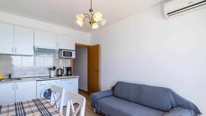 Une cuisine compacte avec des meubles blancs, un four à micro-ondes, un lave-linge et un coin repas agrémenté d’une nappe à carreaux.
