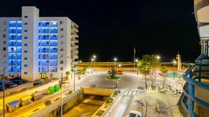 Un hotel de varios pisos con ventanas iluminadas, una glorieta central y un estacionamiento con varios vehículos.