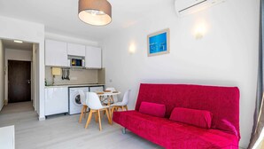 Una sala moderna con un sofá rojo, un comedor con sillas blancas, una cocina con armarios blancos y una lavadora.