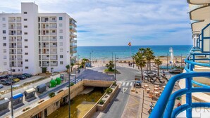 Un hotel costero con varios pisos, una carretera con coches, un paseo peatonal y vistas al mar.