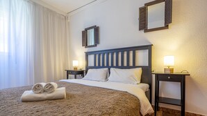Ein Hotelzimmer mit Bett, zwei Nachttischen mit Lampen, einem Kopfteil und einem Fenster mit Vorhängen.