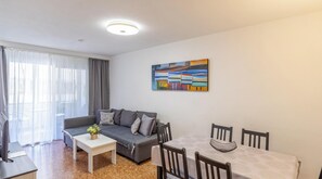 A modern living room with a sofa, a coffee table, a dining table with chairs, a painting on the wall, and a window with curtains. - Inftour Apolo III Apartamento (Calp)