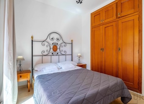 A bedroom with a bed, a nightstand, a lamp, and a wooden wardrobe. - Inftour Medici Apartamento (Calp)