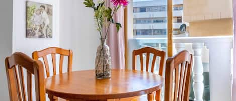 A dining area with a round wooden table and six chairs, a vase with flowers, and two framed pictures on the wall.