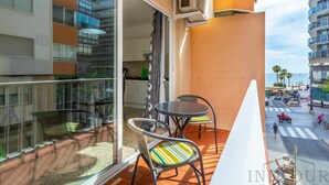 A balcony with two chairs and a table, overlooking a street with vehicles and pedestrians. - Inftour Stefano Apartamento (Calp)