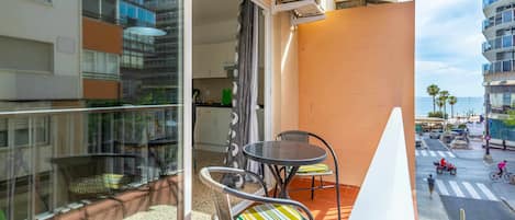Un balcon avec deux chaises et une table, donnant sur une rue où circulent des véhicules et des piétons.