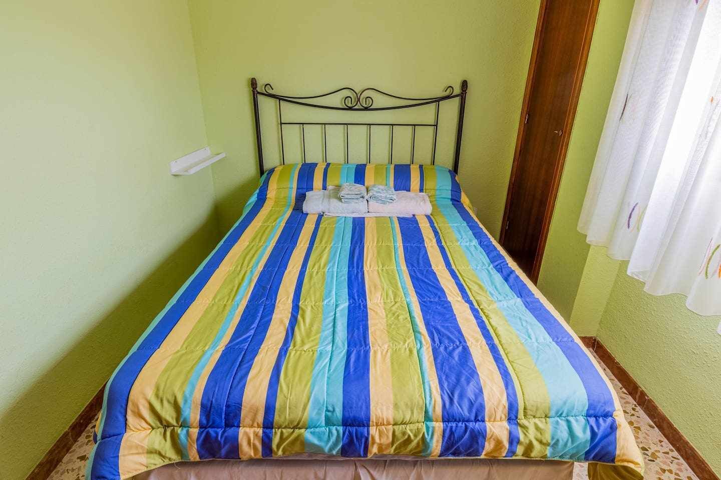 A single bed with a striped bedspread in a room with green walls and a curtain on the window.