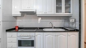 Een keuken met witte kasten, een zwart aanrecht, een fornuis, een spoelbak en een koffiezetapparaat.