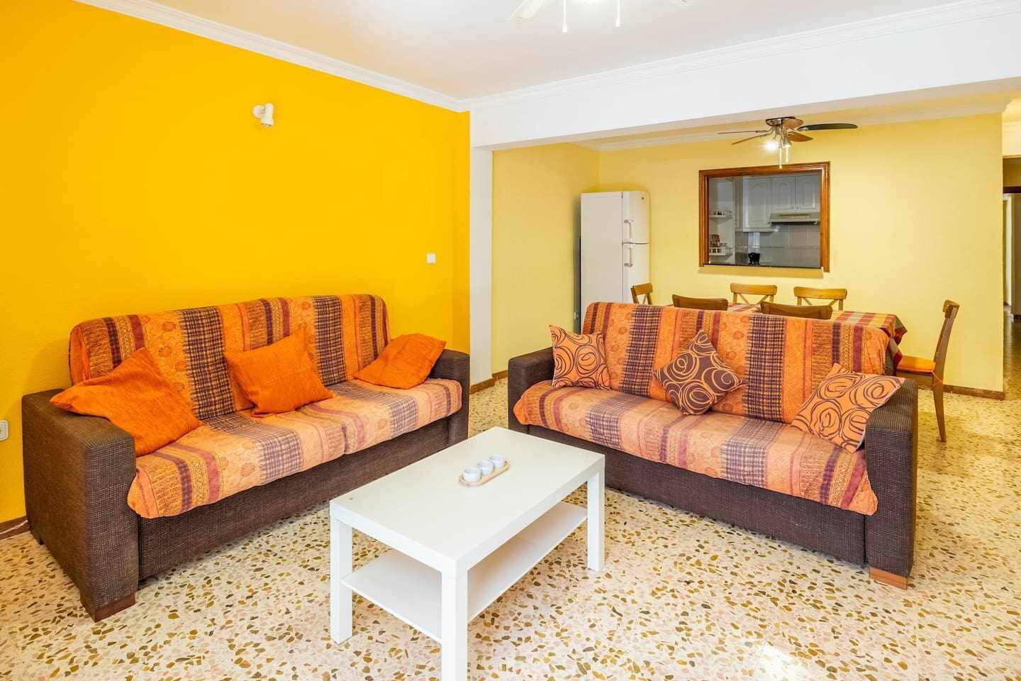 A living room with two sofas, a coffee table, and a dining area with chairs and a table.