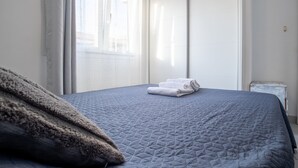 Ein ordentlich bezogenes Bett mit einer gesteppten blauen Decke, zwei gefaltete weiße Handtücher und eine flauschige braune Decke auf der linken Seite.