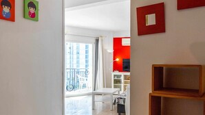 Un appartamento moderno con un corridoio che dà su un balcone. Si notano due quadri rossi appesi al muro, una rastrelliera metallica e un mobiletto a mensole in legno.
