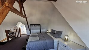 A bedroom with a sloped ceiling, a bed with grey bedding, a bedside table with a lamp, and a white dresser. - Charming townhouse, 10 minutes walk from the beach! (Erquy)