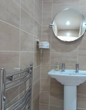 A bathroom with a white sink, a round mirror, and a glass shower enclosure. - Lovely Flat in Birmingham (Birmingham)