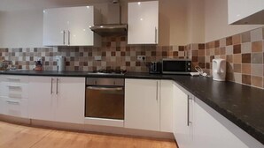 Una cocina moderna con armarios blancos, microondas, hervidor y estufa a gas.
