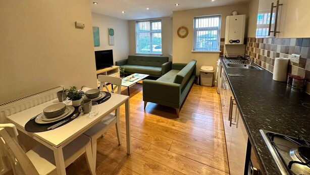 Un espacio habitable compacto con comedor, un sofá verde, una cocina con estufa y un televisor.
