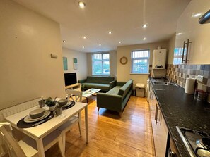 A compact living space with a dining area, a green sofa, a kitchen with a stove, and a TV. - Lovely Flat in Birmingham (Birmingham)