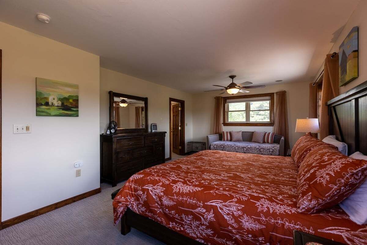 A bedroom with a large bed, a dresser, a ceiling fan, and a window with curtains.