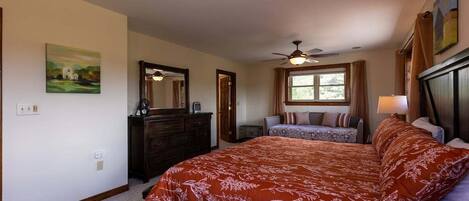 A bedroom with a large bed, a dresser, a ceiling fan, and a window with curtains.