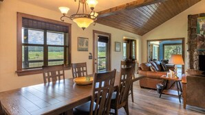 Un espace repas avec une table et des chaises en bois, un lustre et une vue sur l’extérieur grâce à de grandes fenêtres.