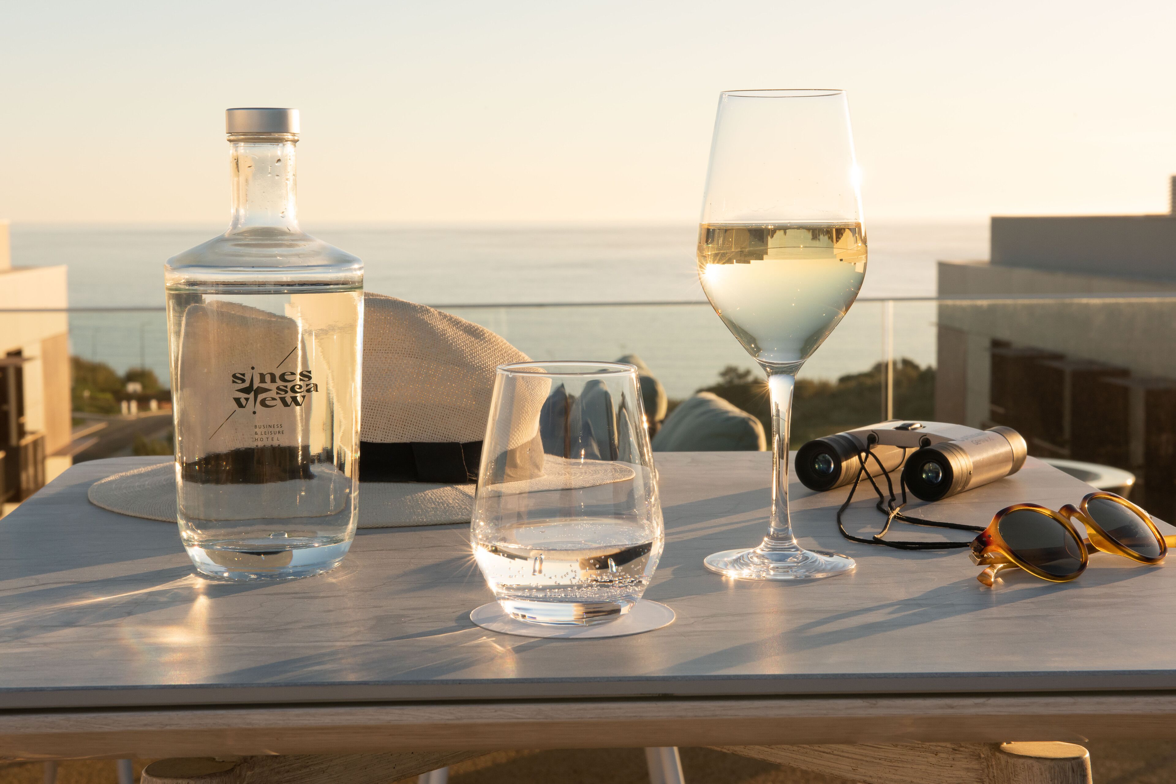 A table with a bottle, two glasses, binoculars, and sunglasses.