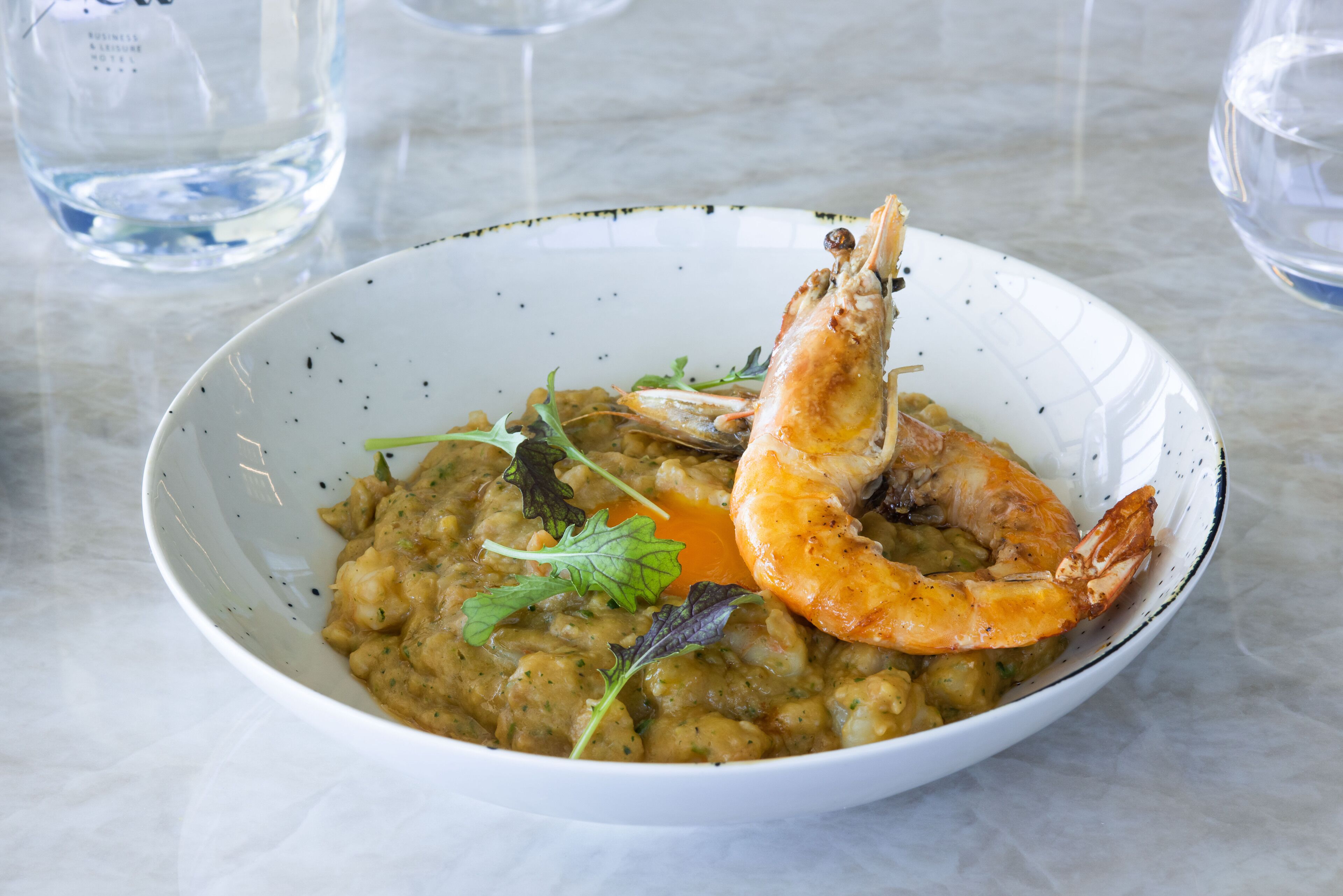 A bowl of food with a shrimp and greens on a marble table.