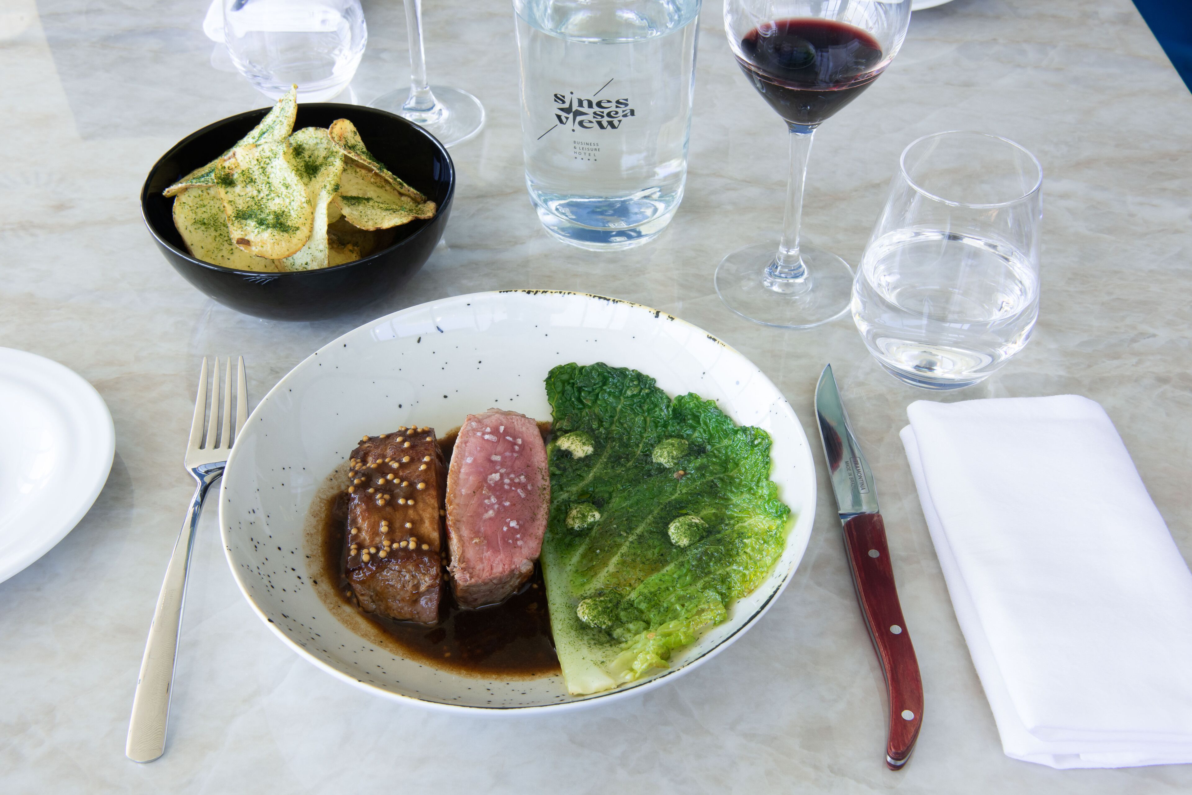 A dining table with a plate of food, a bottle of water, and wine glasses.