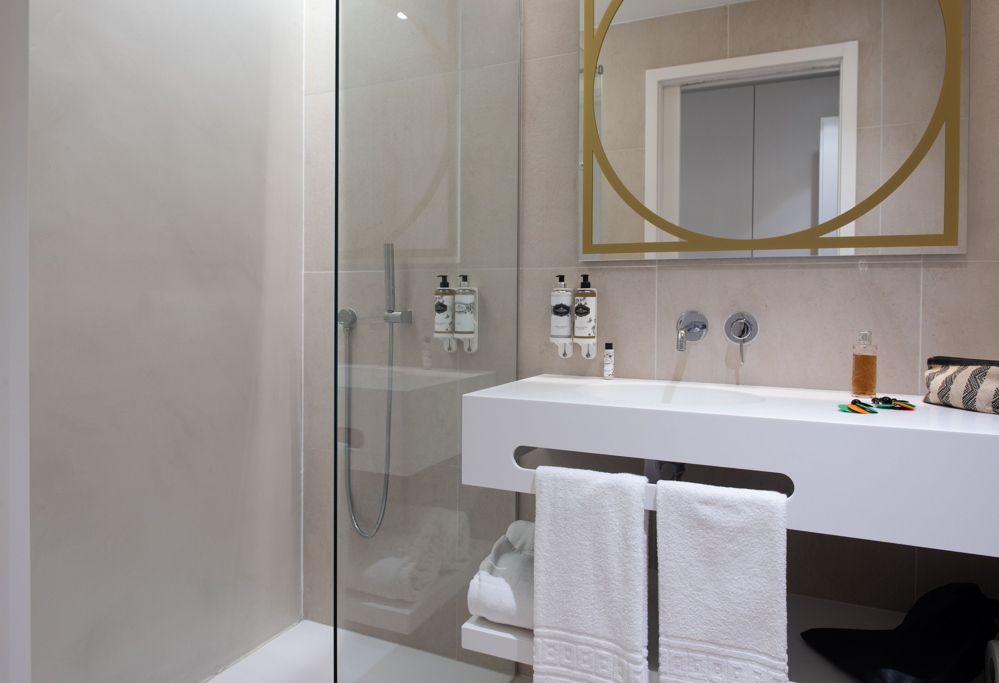 A modern bathroom with a glass-enclosed shower, a white sink with a gold-framed mirror, and neatly folded towels.