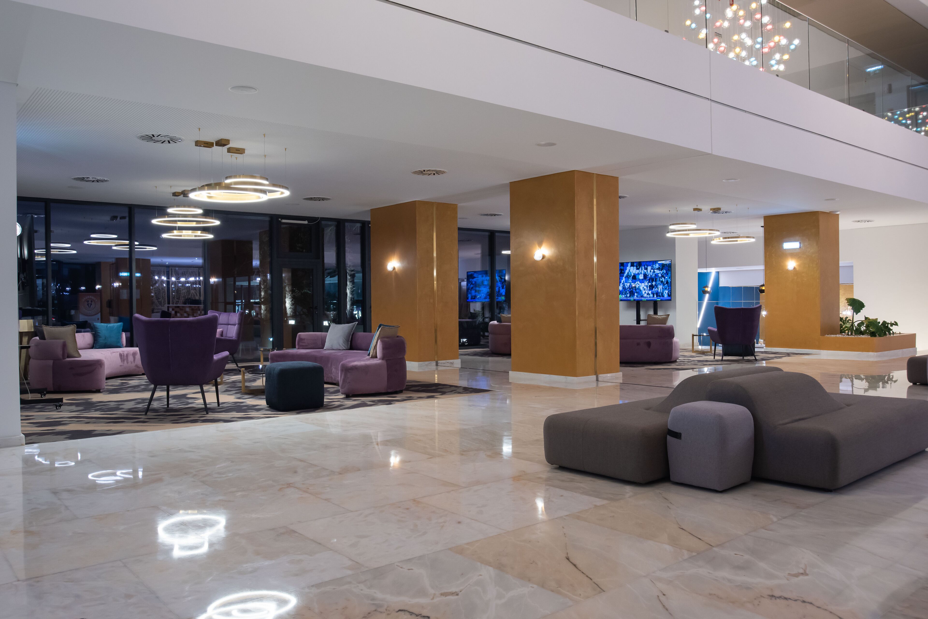 A modern lobby with a polished marble floor, contemporary furniture, and a large flat-screen TV mounted on a wooden pillar.