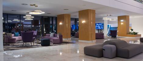 A modern lobby with a polished marble floor, contemporary furniture, and a large flat-screen TV mounted on a wooden pillar.