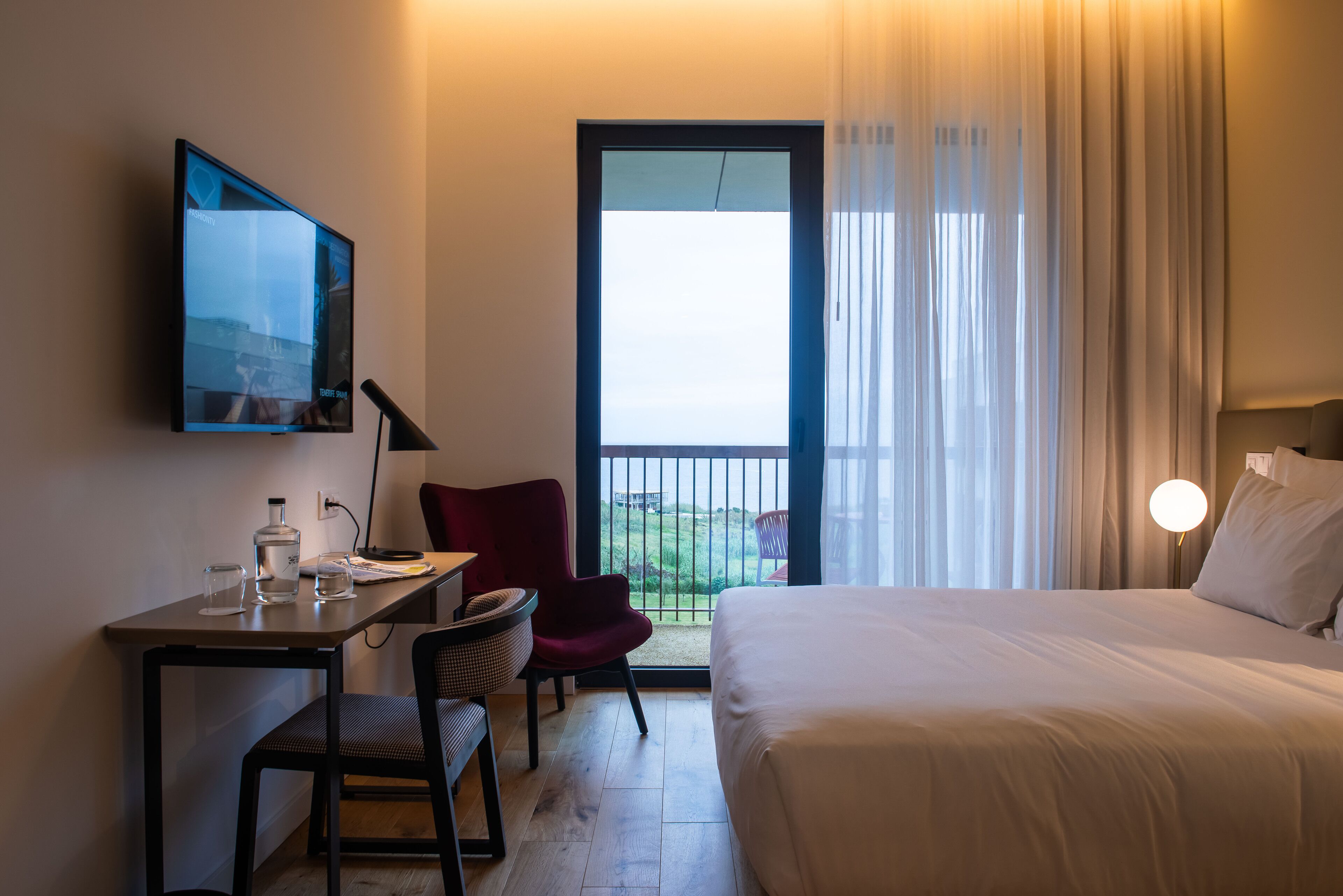 Une chambre d’hôtel comprenant un lit, un bureau avec une chaise, une télévision et une vue sur l’extérieur par une fenêtre.