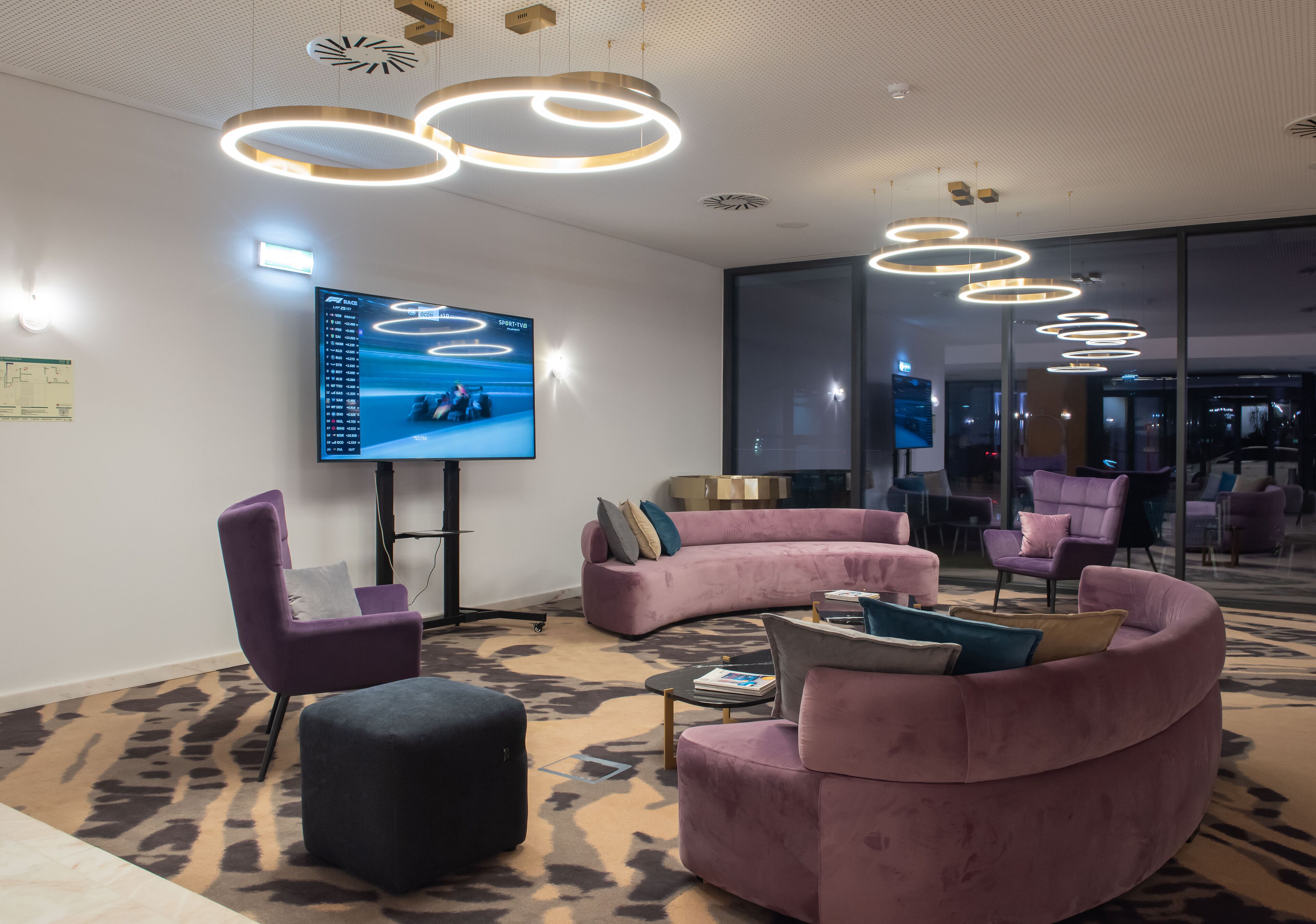 A modern lounge area with a large flat-screen TV, plush seating, and unique circular ceiling lights.
