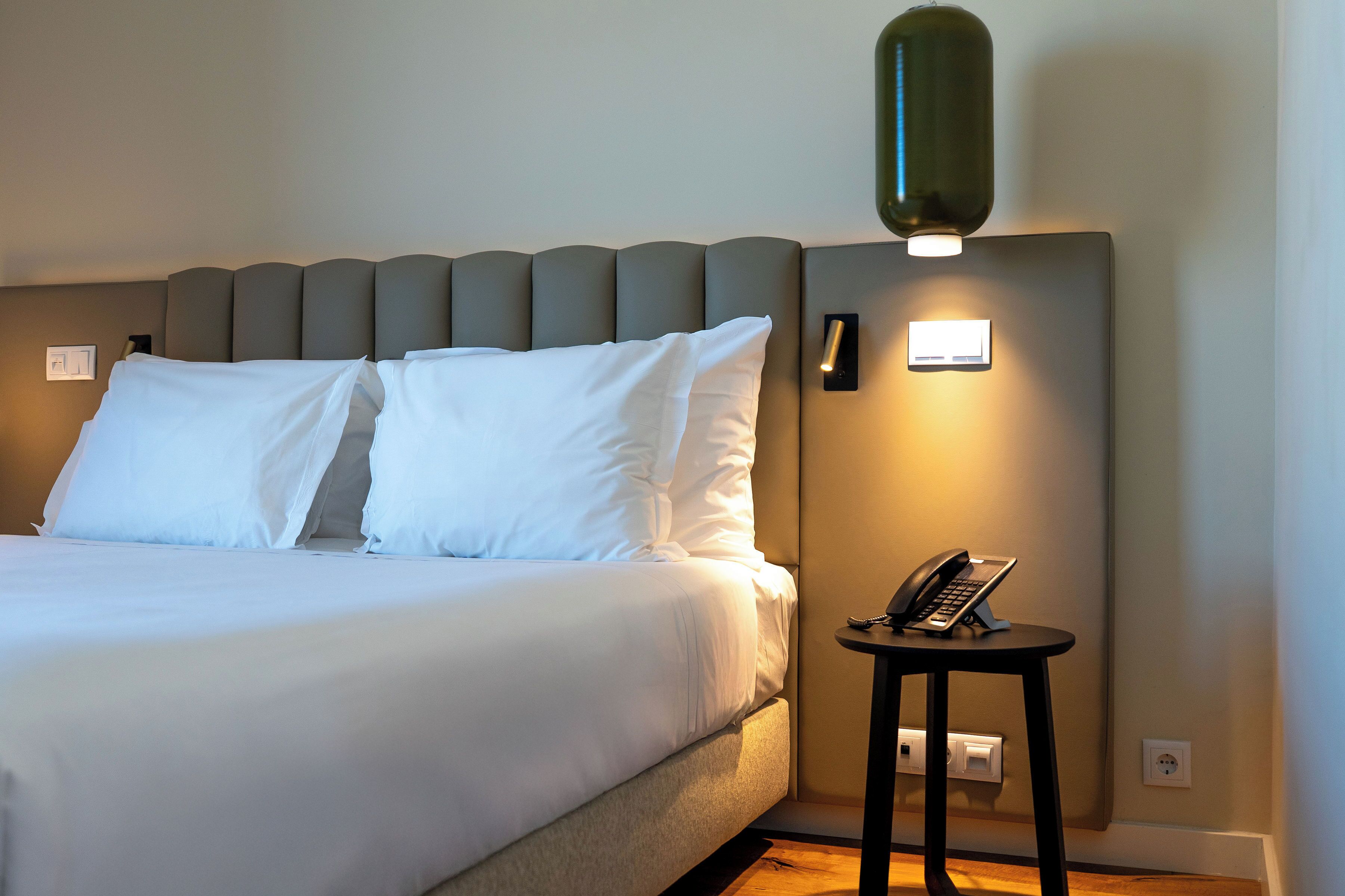 A hotel room with a bed, a bedside table with a telephone, and a wall-mounted light fixture.