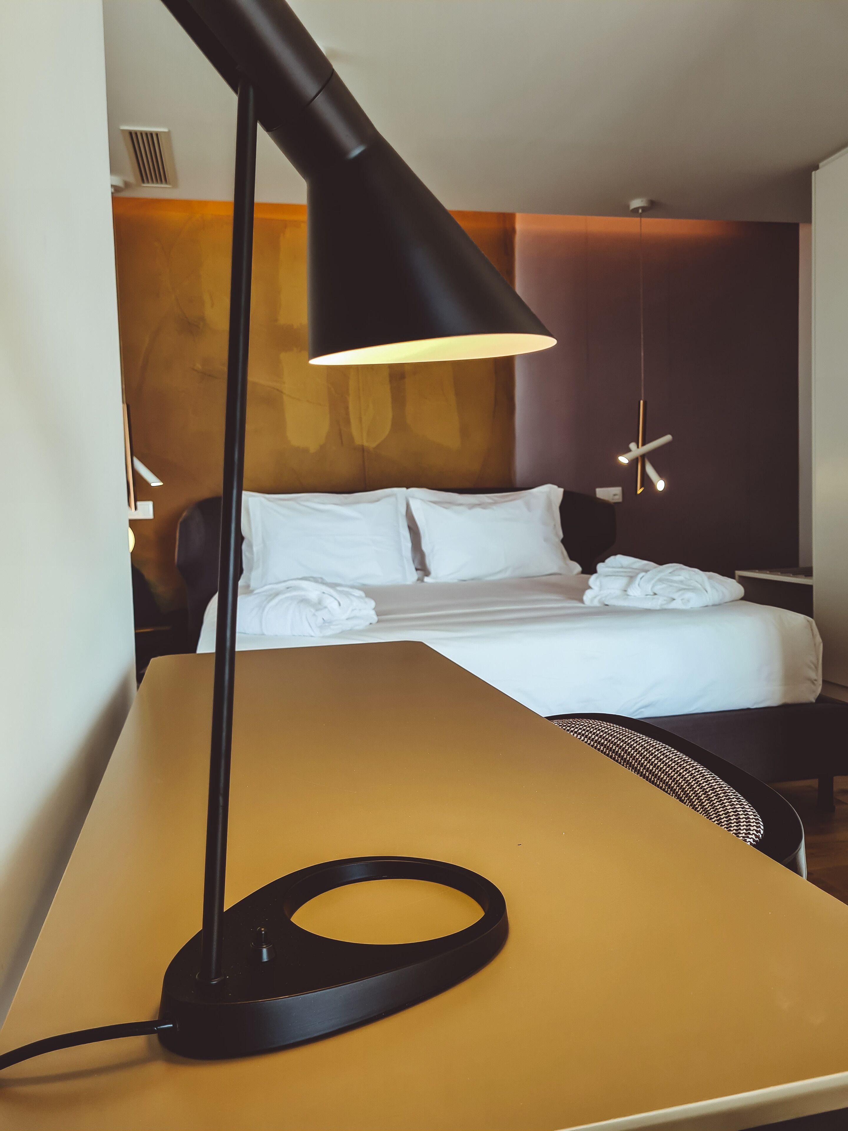Una habitación de hotel con una cama, un escritorio y una lámpara de escritorio negra.