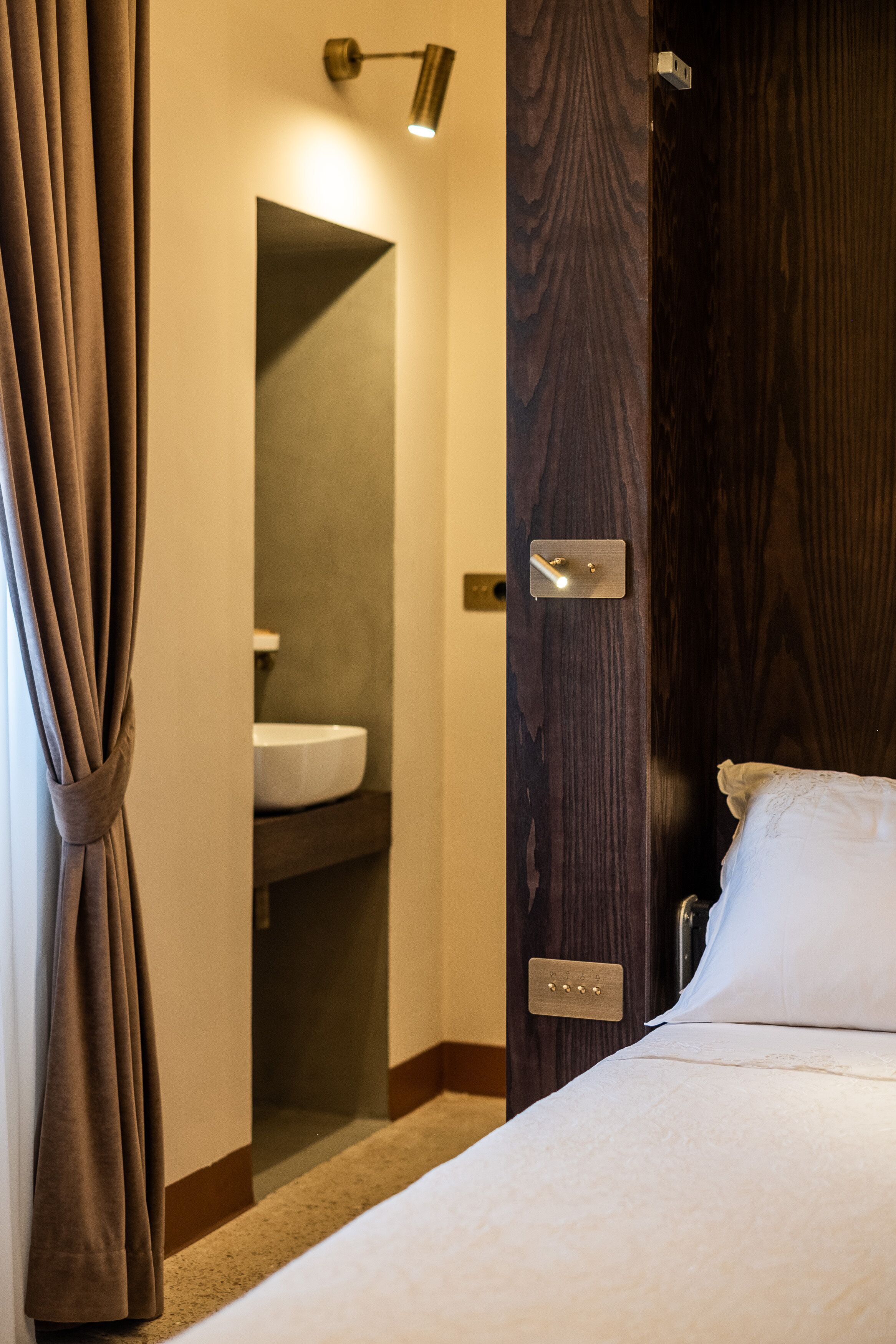 A hotel room with a bed, a wooden door, a bathroom with a sink, and a curtain.