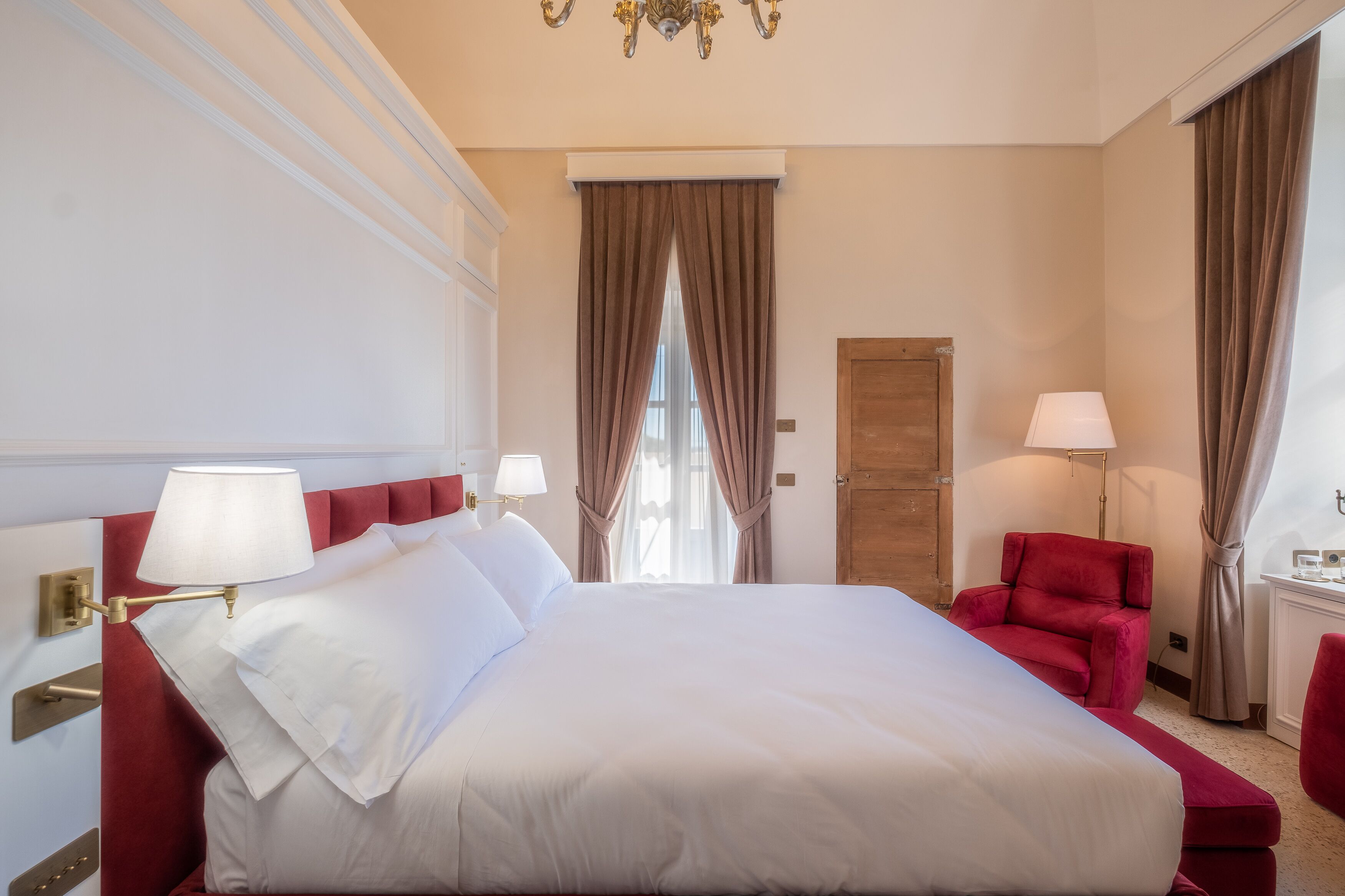 Ein Hotelzimmer mit einem großen Bett, einem roten Sessel und zwei Nachttischlampen.