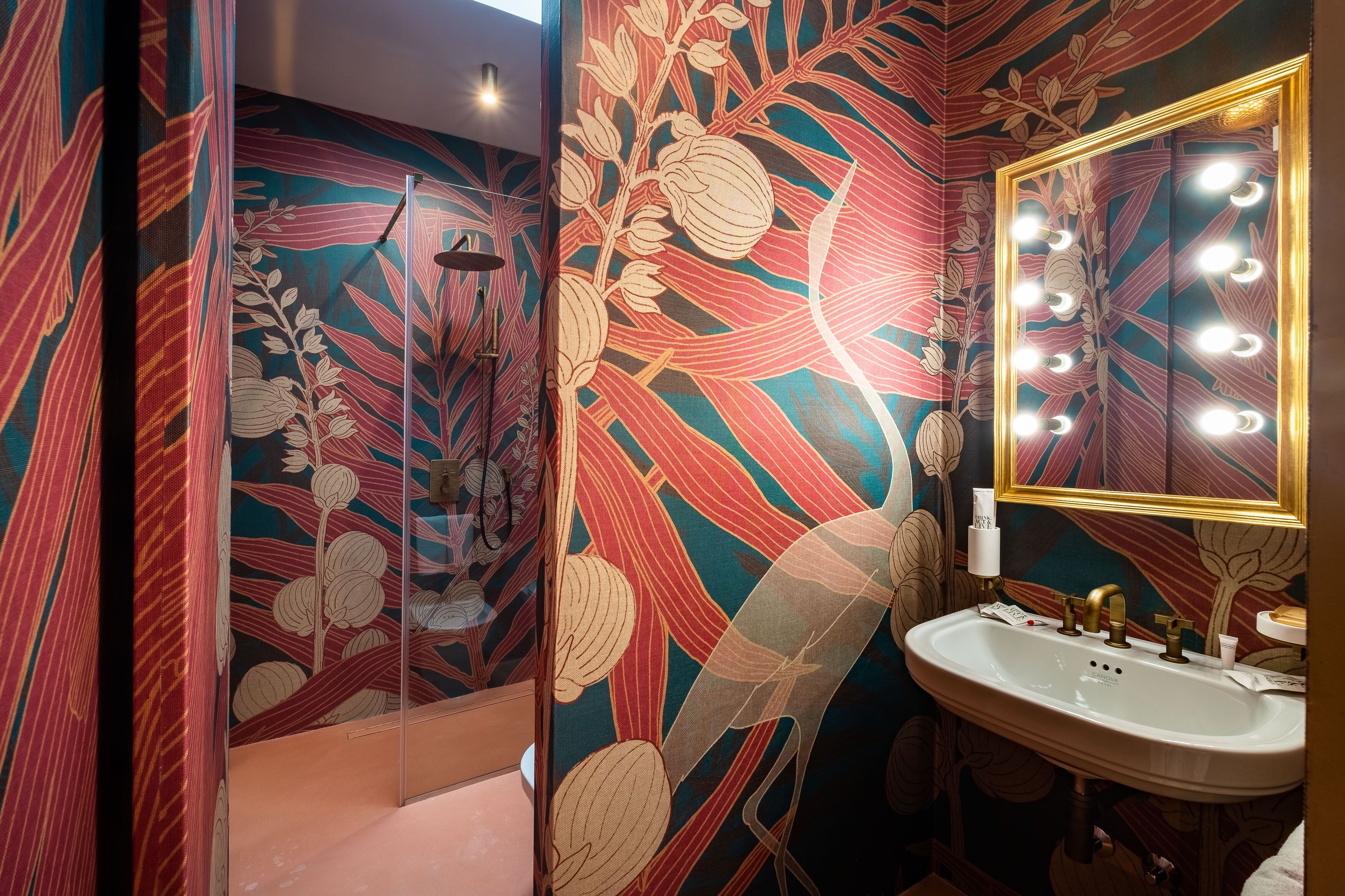 Une salle de bain avec un meuble-lavabo, un miroir avec éclairage intégré et un espace douche agrémenté d’un motif floral sur le mur.