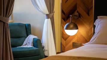 Ein Hotelzimmer mit einem Bett, einem grünen Sessel, einer Wandleuchte und Vorhängen.