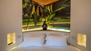 Un dormitorio con una cama, dos mesitas de noche y una ventana con vistas a un jardín y un edificio.