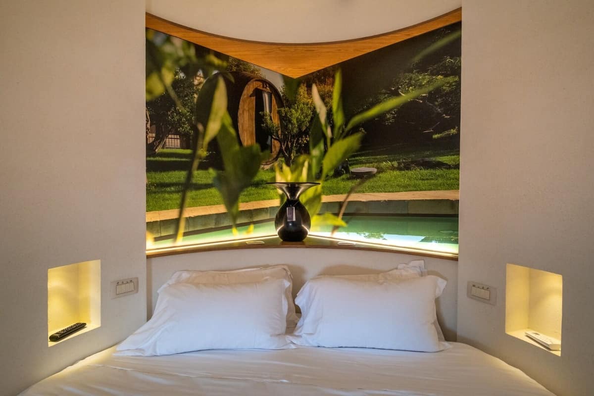 Un dormitorio con una cama, dos mesitas de noche y una ventana con vistas a un jardín y un edificio.