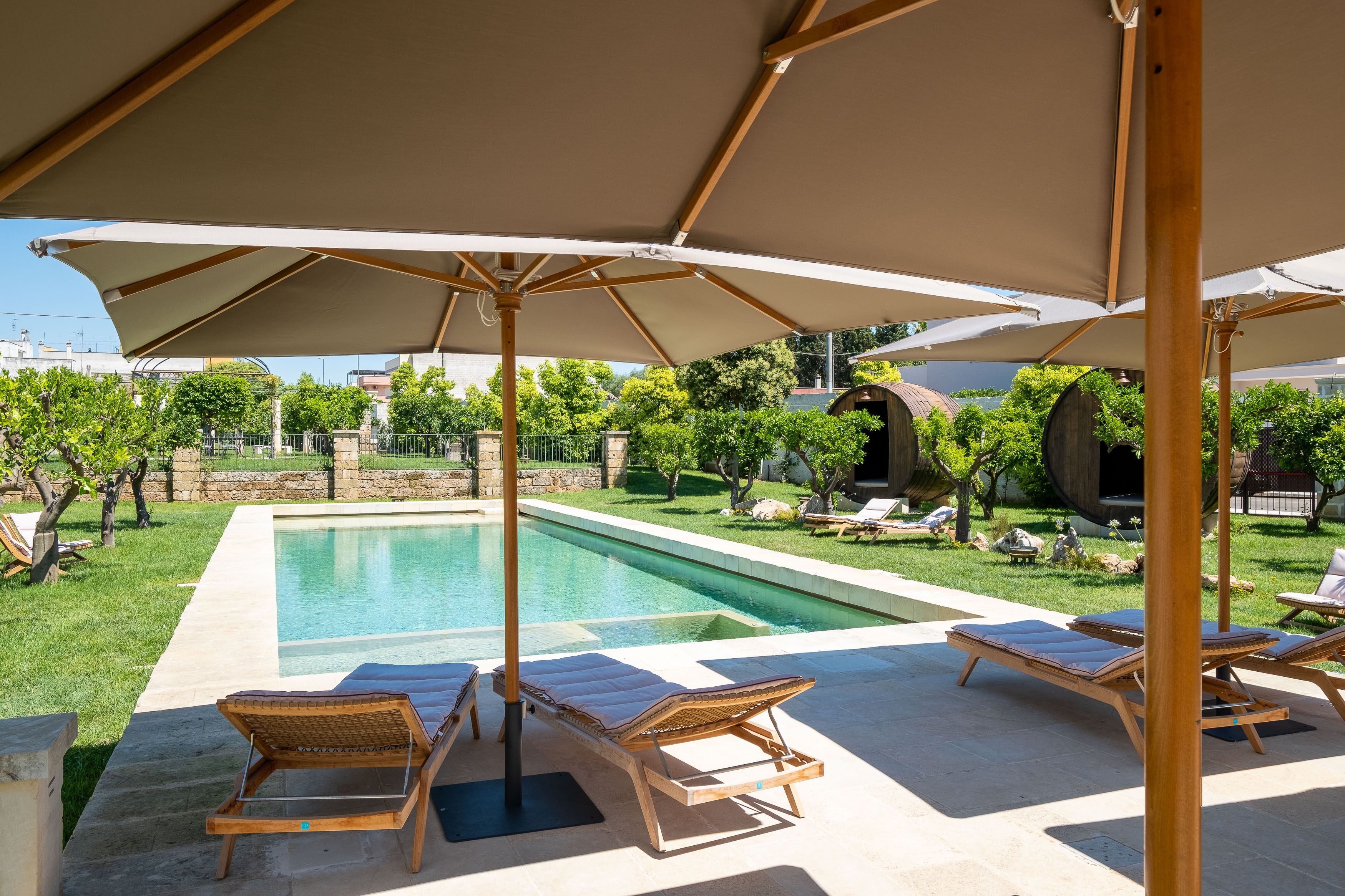 Un espace aménagé au bord de la piscine, avec des chaises longues et des parasols, entouré de verdure et d’un mur en pierre.