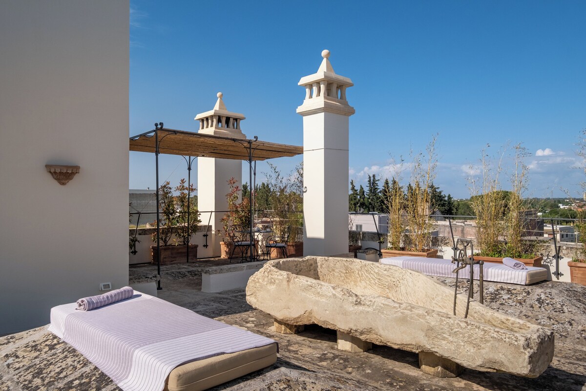A rooftop terrace with a stone bench, a covered seating area, and a view of the cityscape.