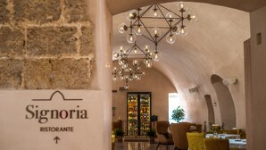Un interior de restaurante con pared de piedra, una araña y mesas dispuestas para comer.