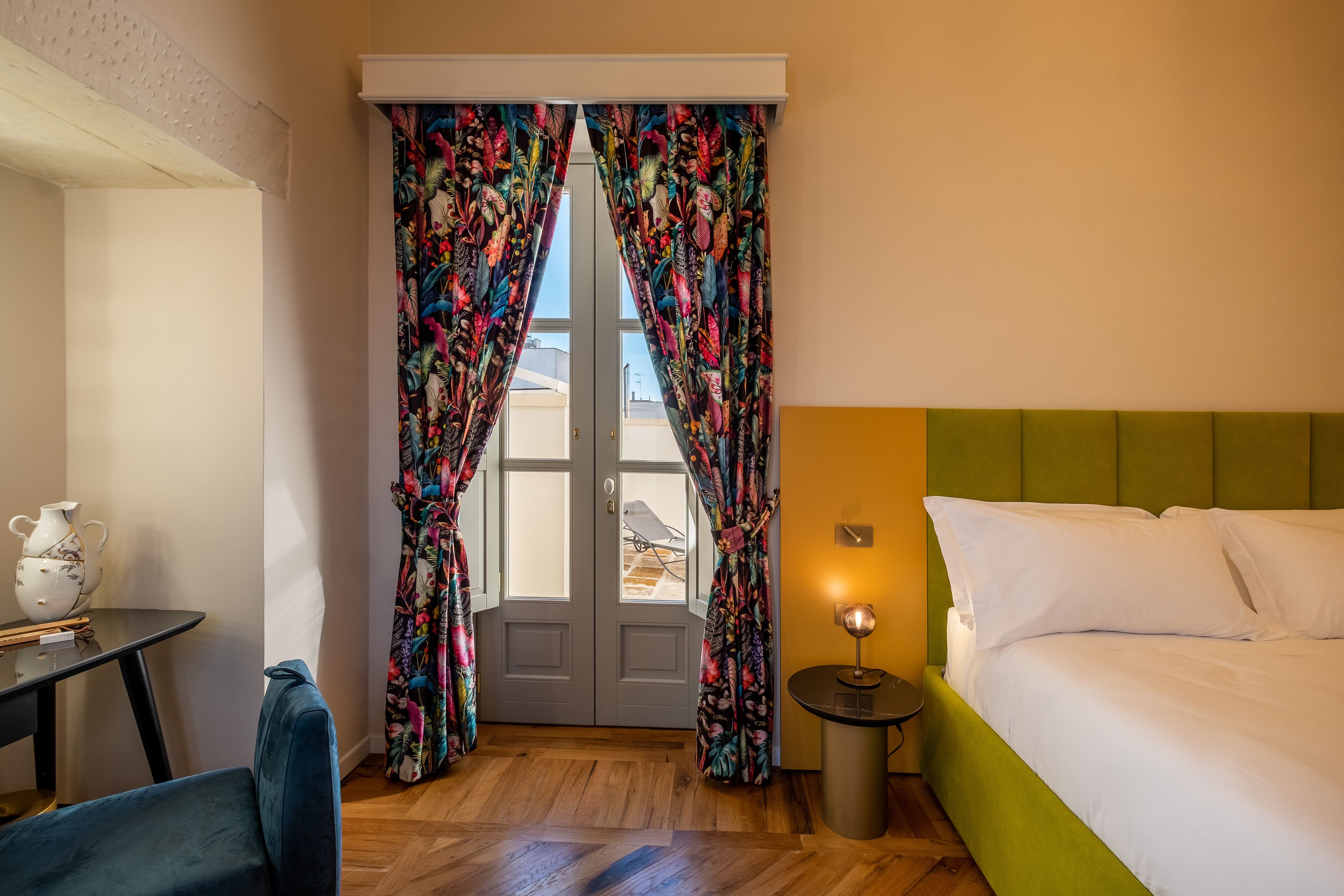 Een kamer met een bed, een tafel met een karaf, gordijnen en een lamp.