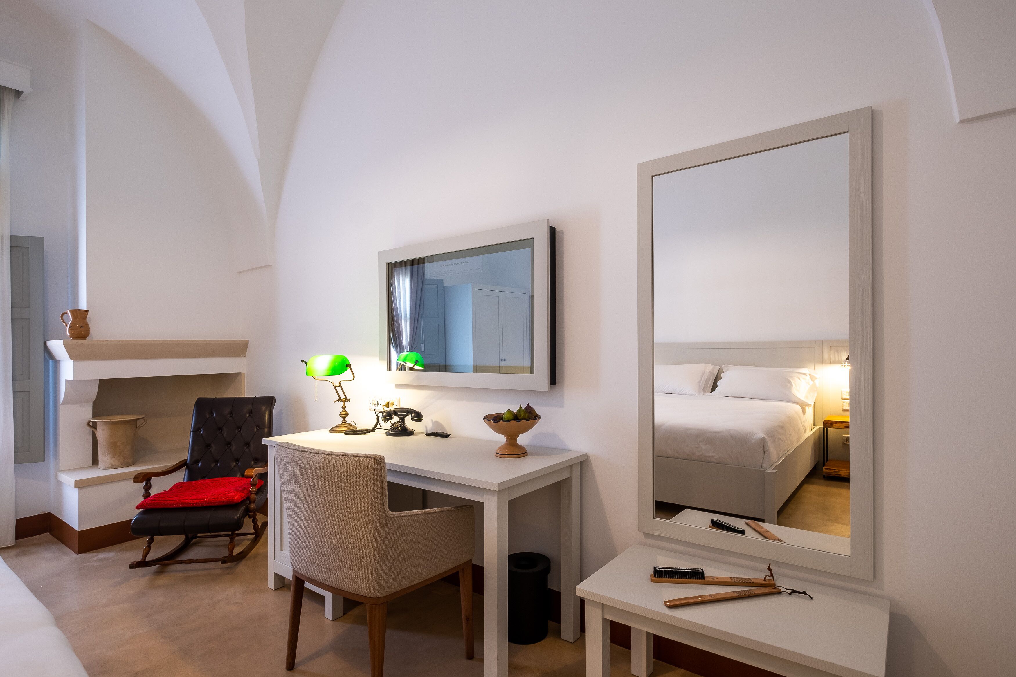 Een hotelkamer met een bed, een bureau met stoel, een spiegel en een tafeltje met lamp.