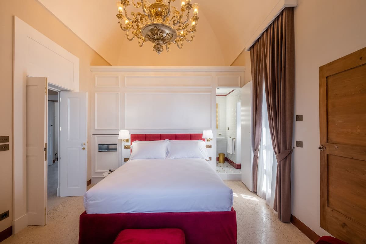 Una habitación de hotel con una cama grande, un candelabro, una puerta de madera y un espejo.
