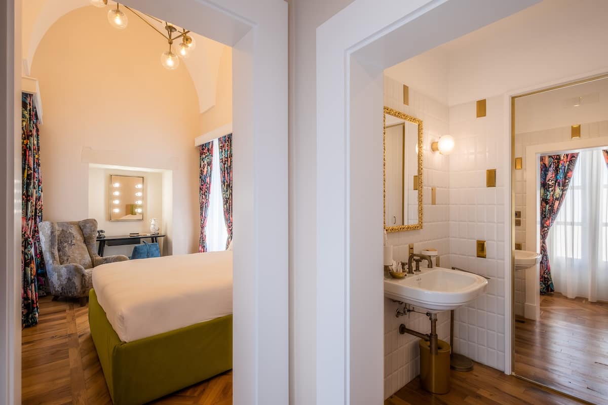 Una habitación de hotel con una cama, un tocador con espejo, un lavabo y una silla.