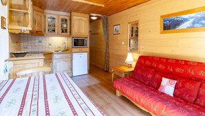 A cozy cabin interior with a kitchen, a dining area, and a living room with a red sofa.