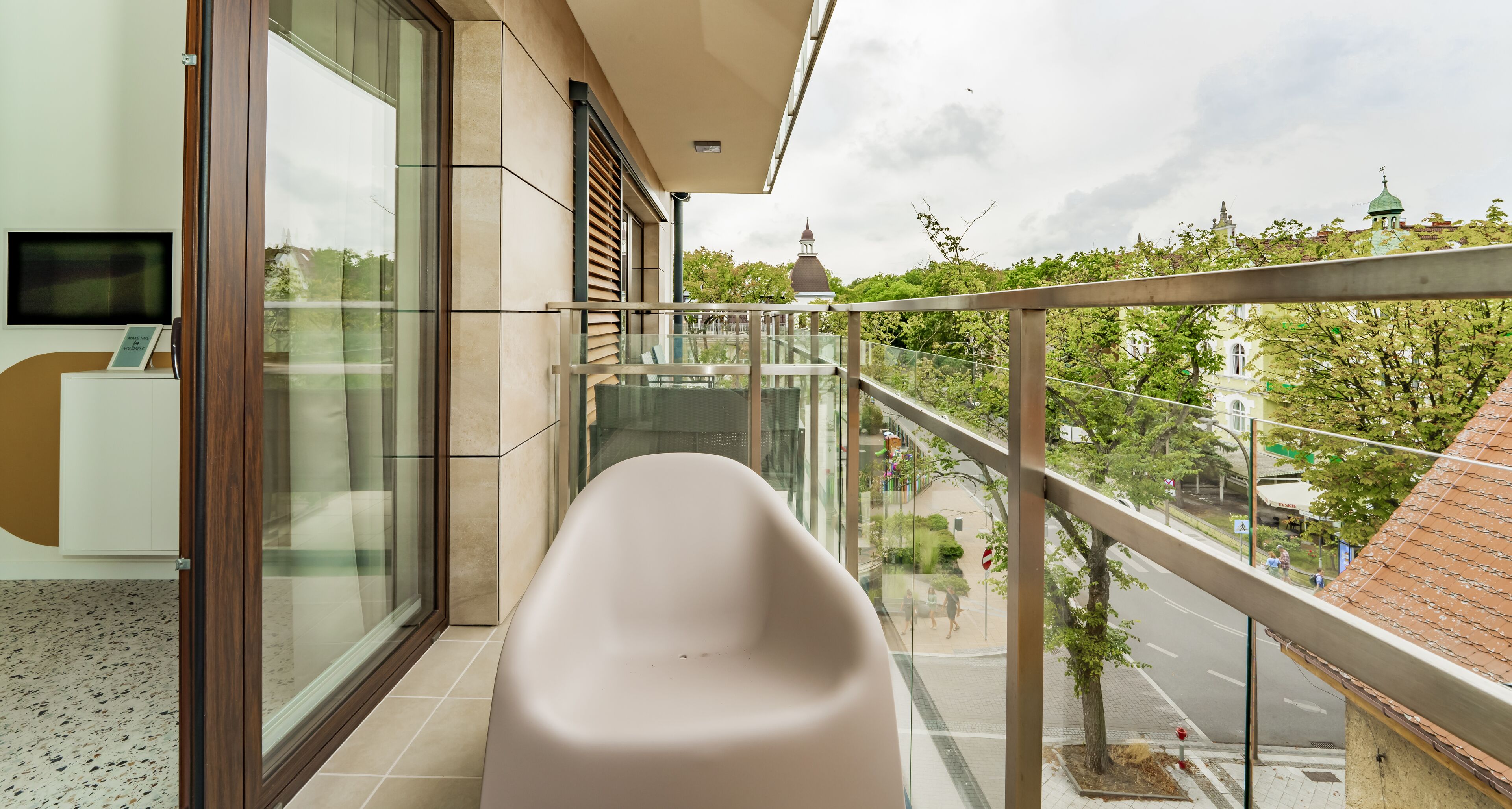 A balcony with a white bathtub, a glass door, and a view of a street and buildings.