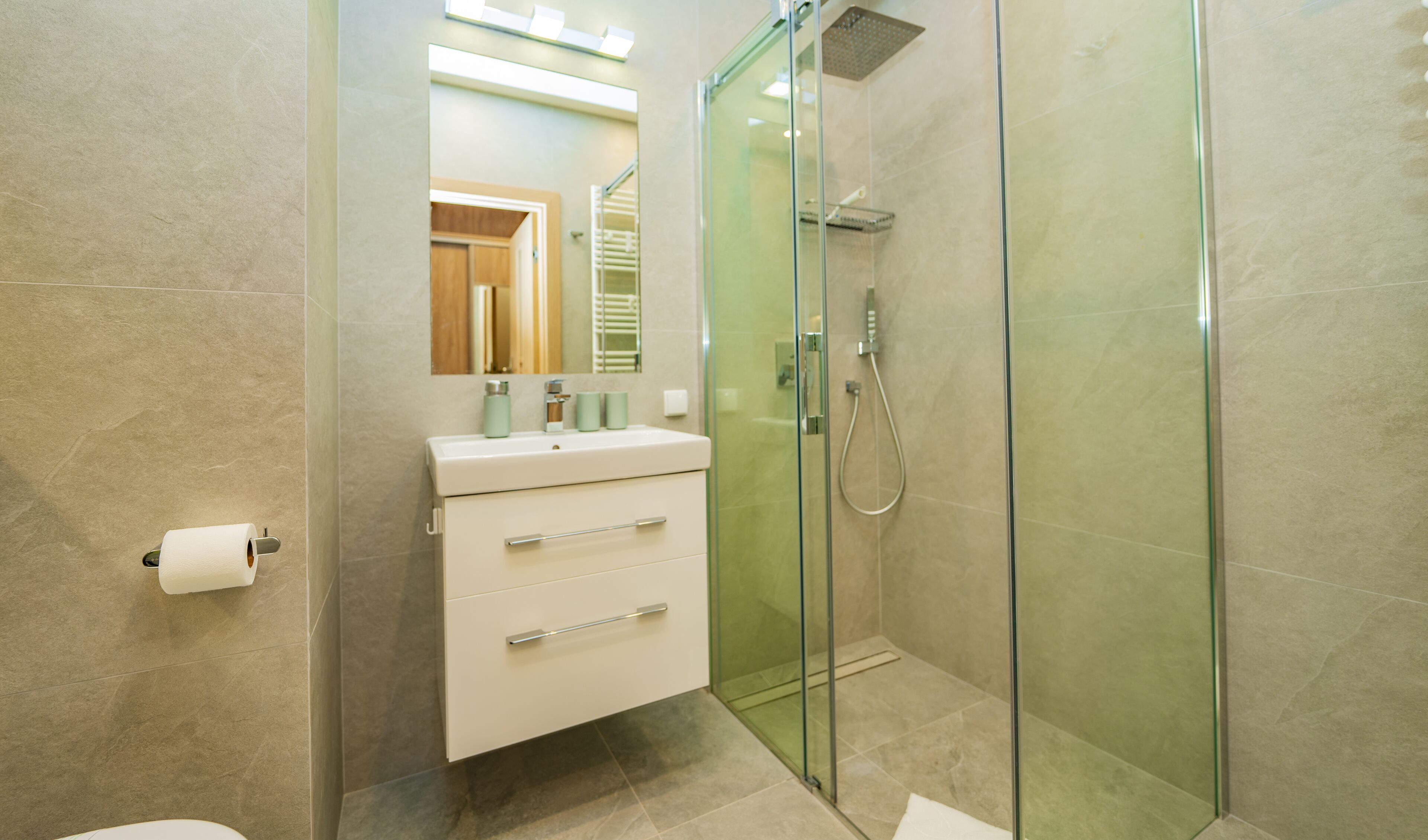 Un baño moderno con ducha envuelta en vidrio, un lavamanos blanco con un espejo encima y un inodoro.