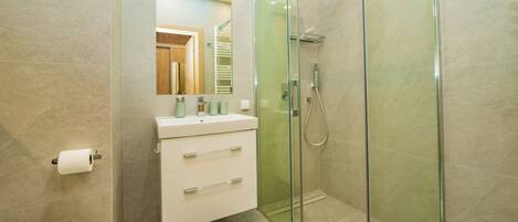 Un baño moderno con ducha envuelta en vidrio, un lavamanos blanco con un espejo encima y un inodoro.